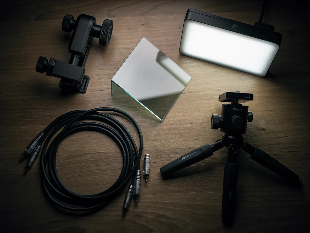 Overhead view of video gear on a wooden desk: phone clamp, angled glass, mini tripod, cables, and a small LED panel.